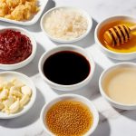 Vibrant gochujang glaze ingredients in white bowls, including gochujang paste, soy sauce, honey, rice vinegar, minced garlic, sesame oil and grated ginger, 3D food photography for high-protein gochujang chicken tikka bowl recipe