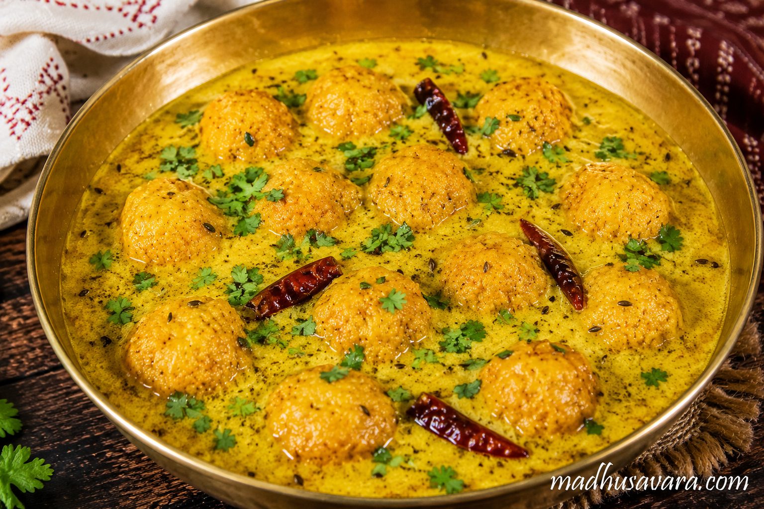 Authentic Boor ki Kadi served in a traditional brass bowl, featuring soft besan boor dumplings in tangy Himachali yogurt gravy, garnished with coriander leaves and whole red chillies, a classic Kangri Dham delicacy