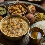 Traditional Himachali Channa Madra served in a brass bowl on a leaf plate during Kangra Dham, accompanied by rice and other authentic Dham dishes.