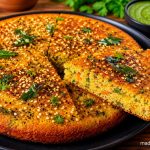 Gujarati Handvo Recipe: Authentic Crispy Lentil and Rice Cake from Gujarat 1 Authentic Gujarati Handvo with crispy sesame crust served on a black plate alongside green chutney and red garlic chutney, showcasing its soft vegetable-filled interior.