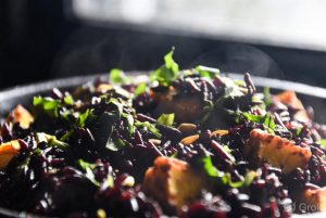 Close-up view of Purple Glow Black Rice Chaulai Paneer Pulao featuring glossy black rice, golden grilled paneer cubes, fresh chaulai (amaranth) leaves, herbs, and seeds with gentle steam rising from the hot dish.