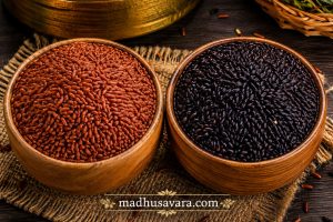 Red rice and black rice displayed in wooden bowls showing the natural colour difference between these traditional whole-grain rice varieties rich in fibre, antioxidants, and nutrients
