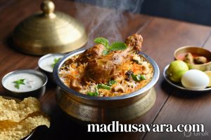 Authentic Malabar Chicken Biryani served in traditional brass handi on a wooden table, garnished with fried onions, cashews, mint and accompanied by raita, boiled egg, lemon and papad - vibrant Kerala style Thalassery biryani