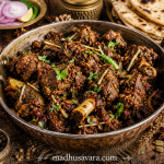 Traditional Ranjha Gosht served in a rustic brass handi, featuring slow-cooked dry mutton coated in rich Punjabi spices with tandoori roti, onions and whole spices.